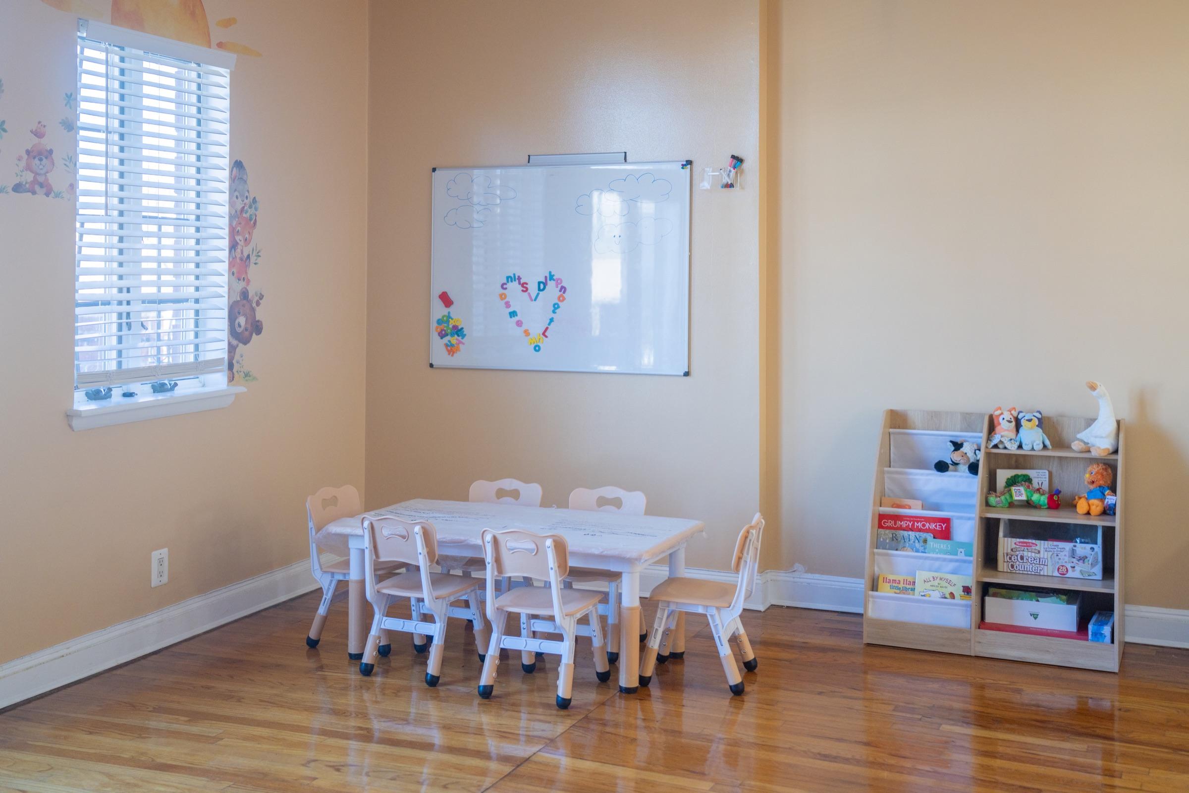 Child-sized table beside books and a whiteboard inside the daycare.
